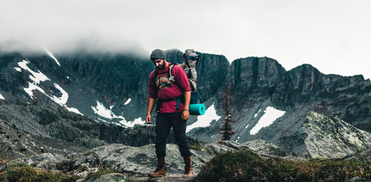 man in red jacket and black pants standing on rocky mountain during daytime